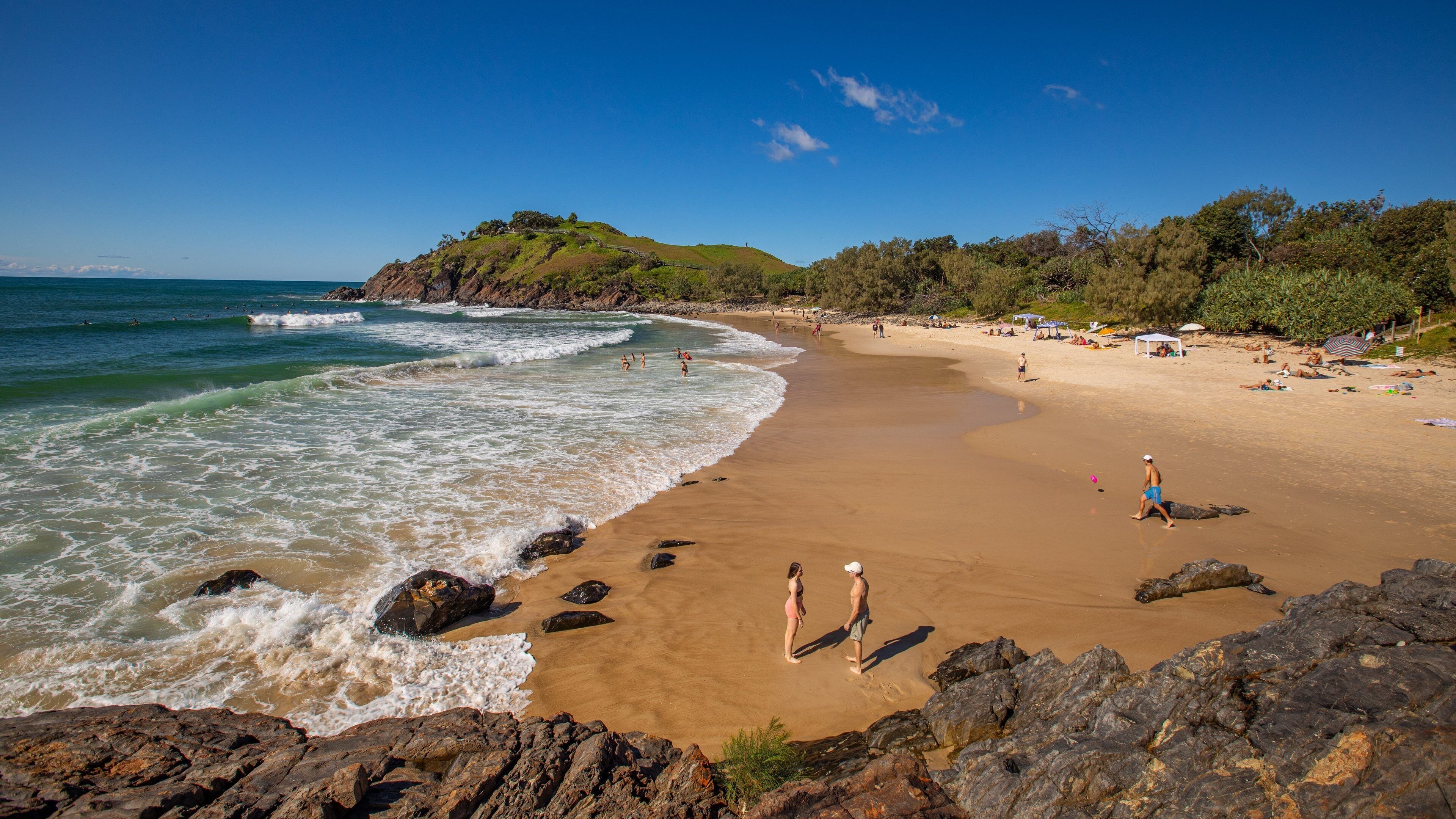A sandy beach with waves, rocky outcrops, and a forested hillside.