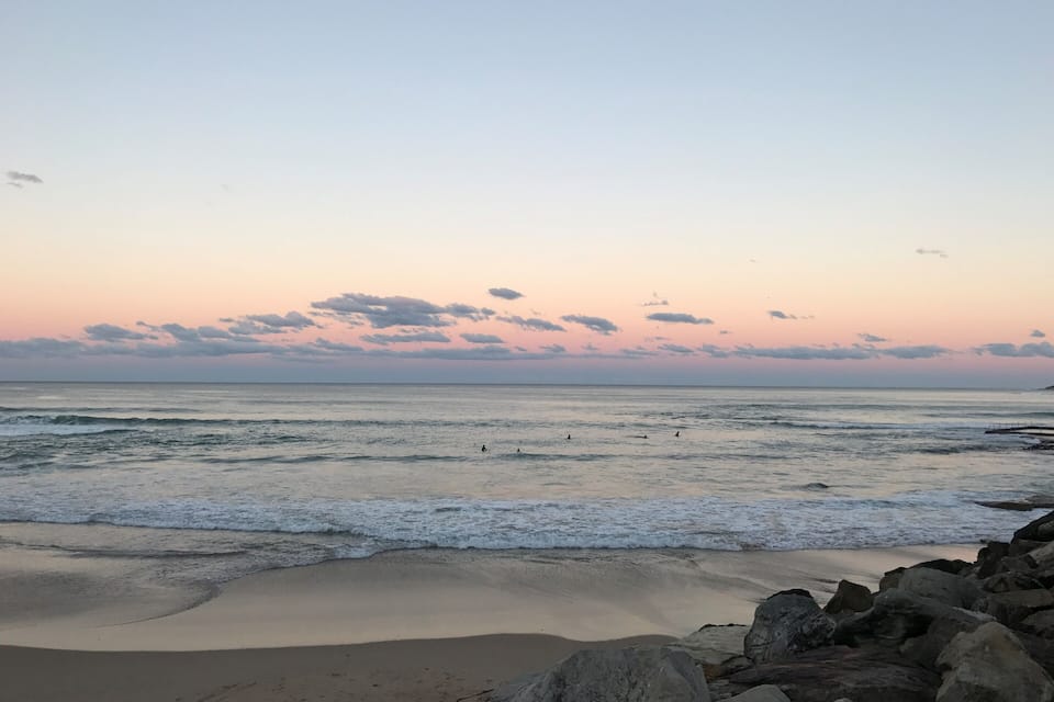 Una playa con olas, rocas y un cielo al atardecer.