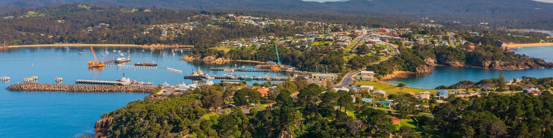 A coastal town with a marina, rocky coastline, and surrounding hills.