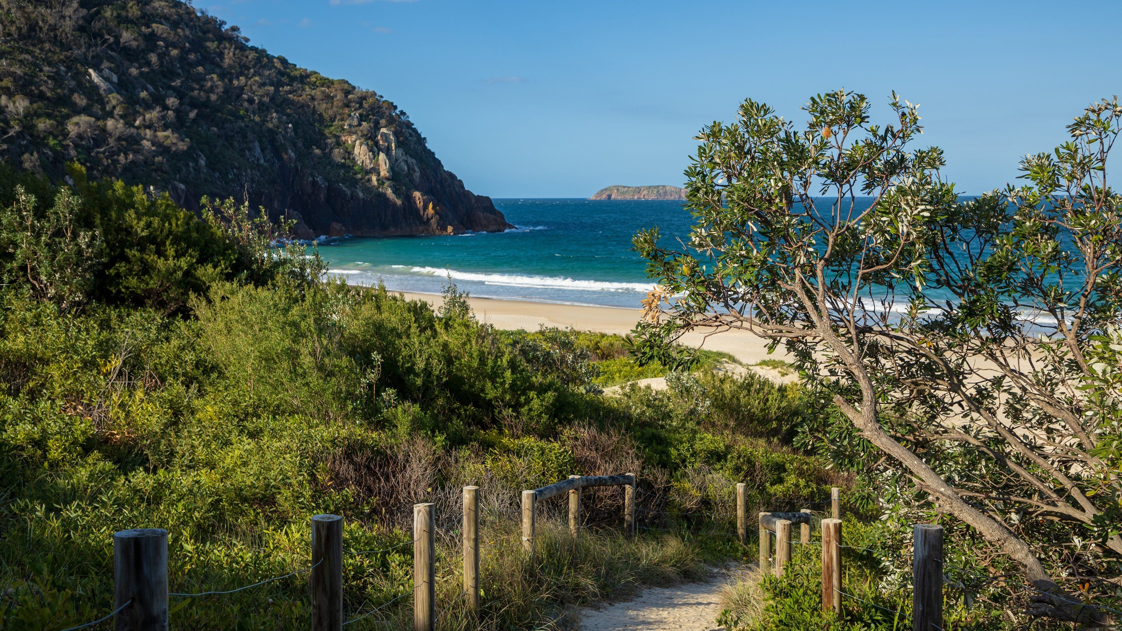 A coastal path leading to a beach with a mountain backdrop and a distant island.