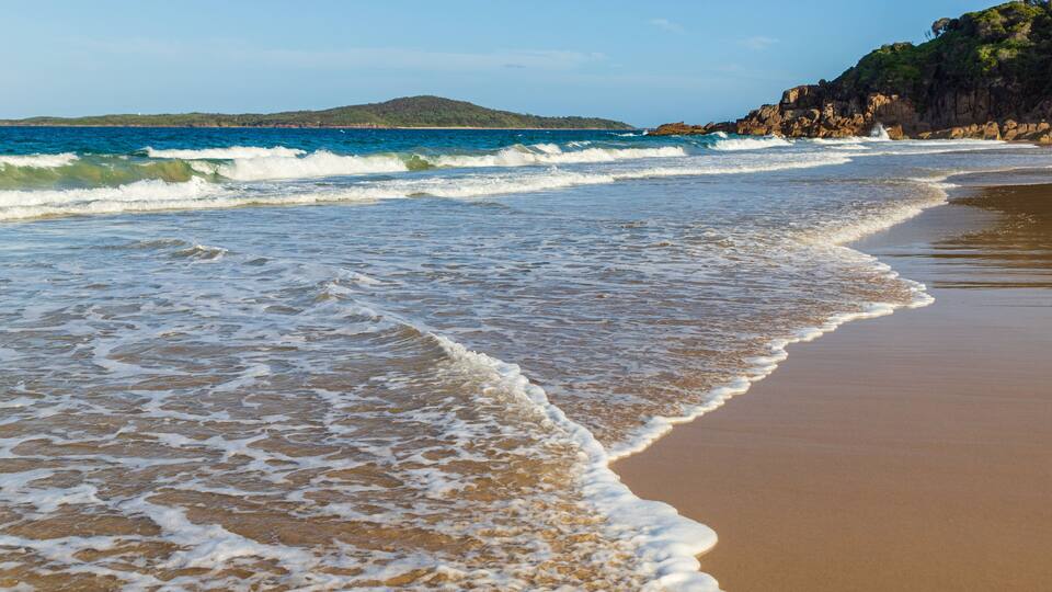 A sandy beach with gentle waves and a rocky coastline.
