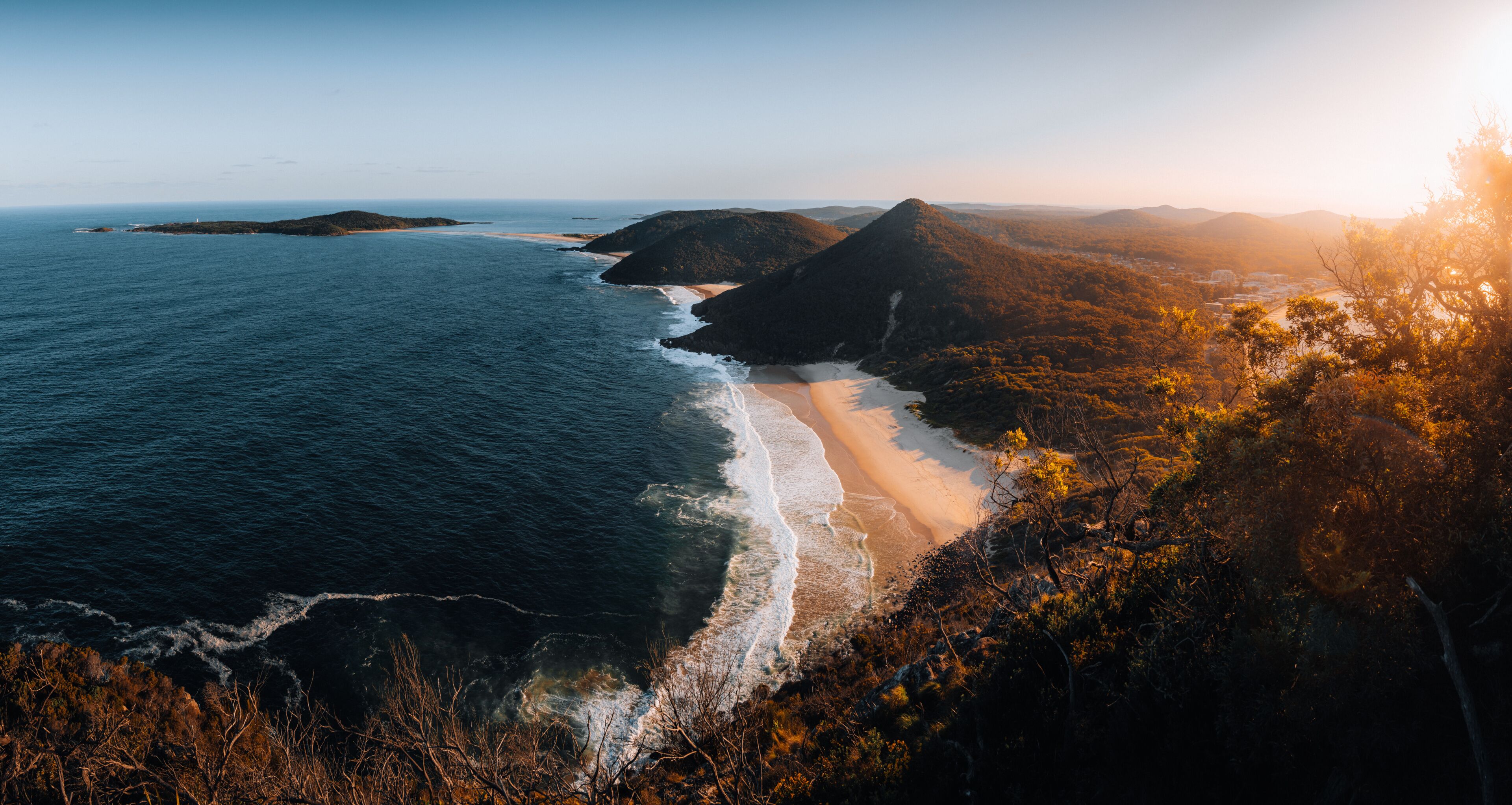 A coastal landscape with a beach, ocean, and forested hills.