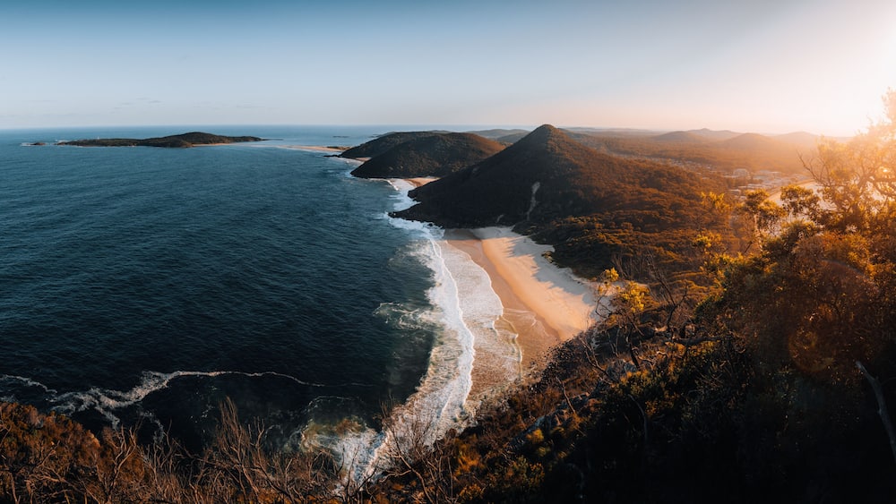 A coastal landscape with a beach, ocean, and forested hills.