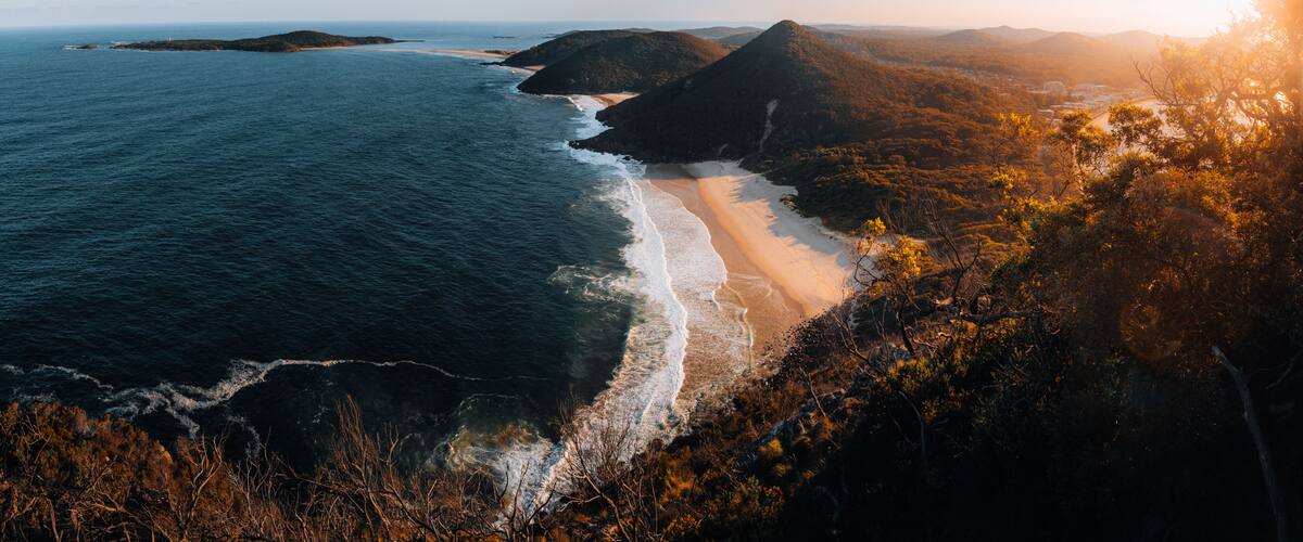 A coastal landscape with a beach, ocean, and forested hills.
