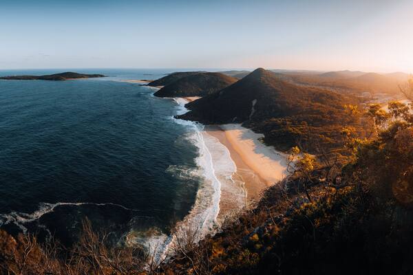 A coastal landscape with a beach, ocean, and forested hills.