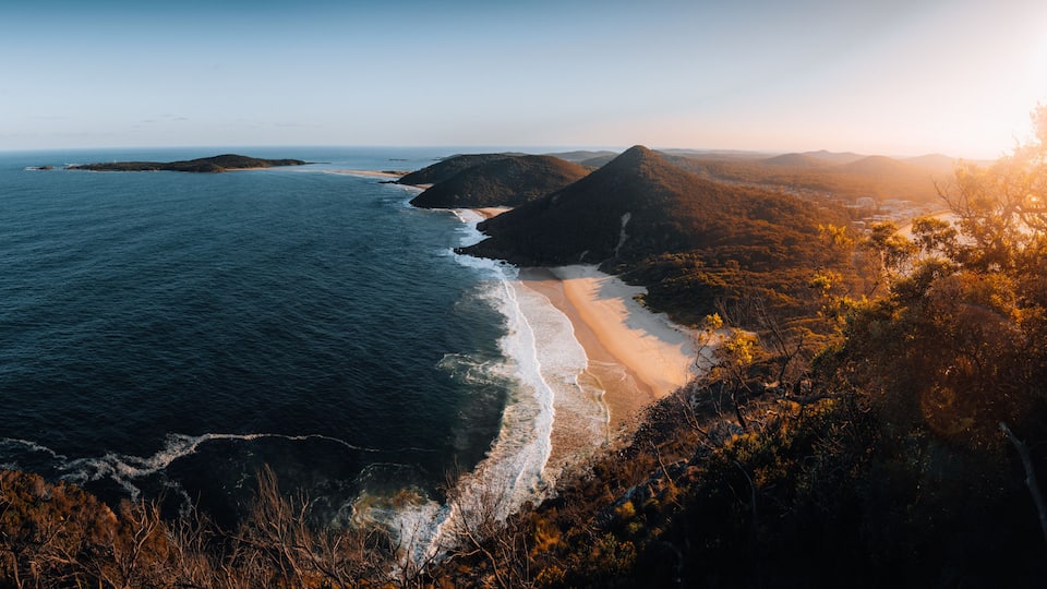 A coastal landscape with a beach, ocean, and forested hills.