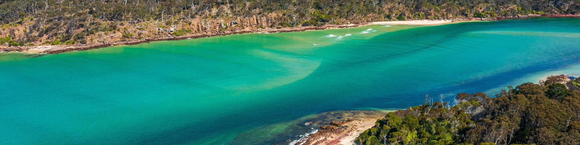 Un paisaje costero con aguas turquesas cristalinas, una playa de arena y una colina boscosa al fondo.
