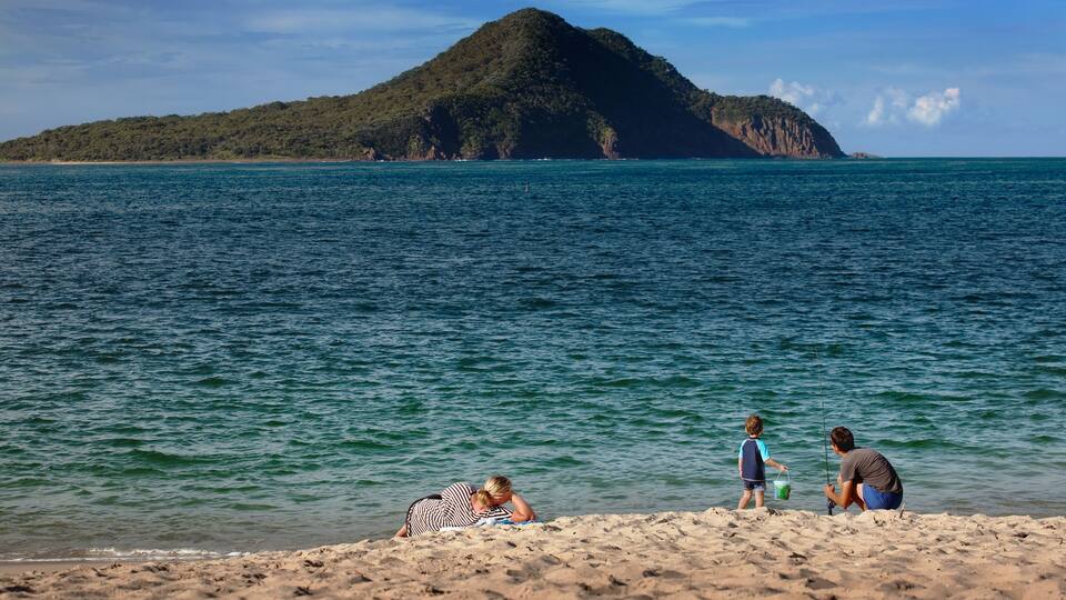 A beach with a person fishing, a child playing, and a woman sunbathing.