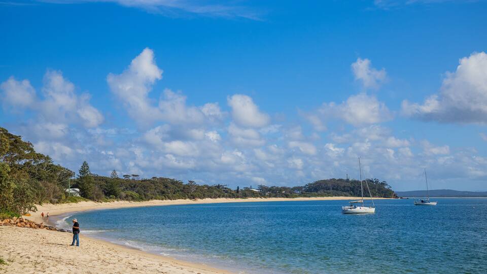 A beach with clear blue water, a sandy shore, and a few boats.
