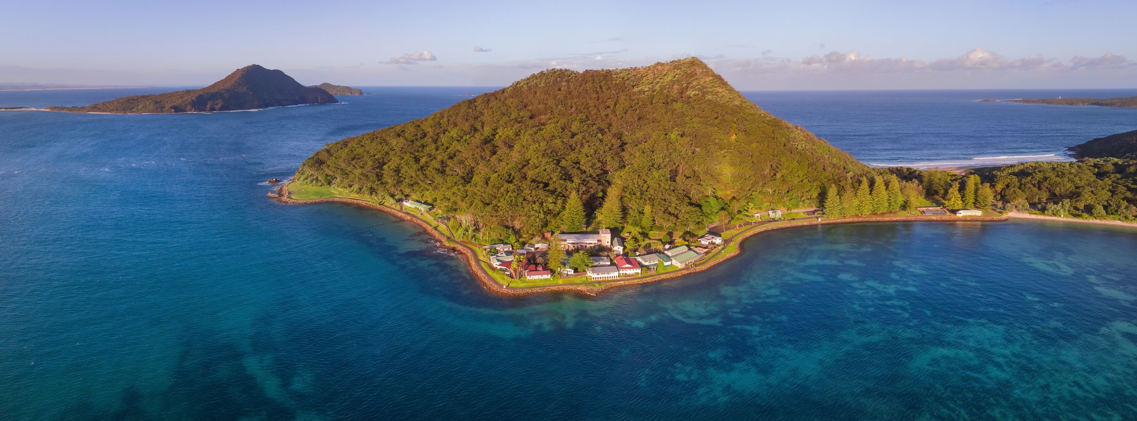 An island with a dense forest, a small settlement, and clear blue waters.