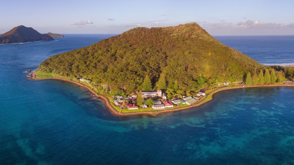 An island with a dense forest, a small settlement, and clear blue waters.