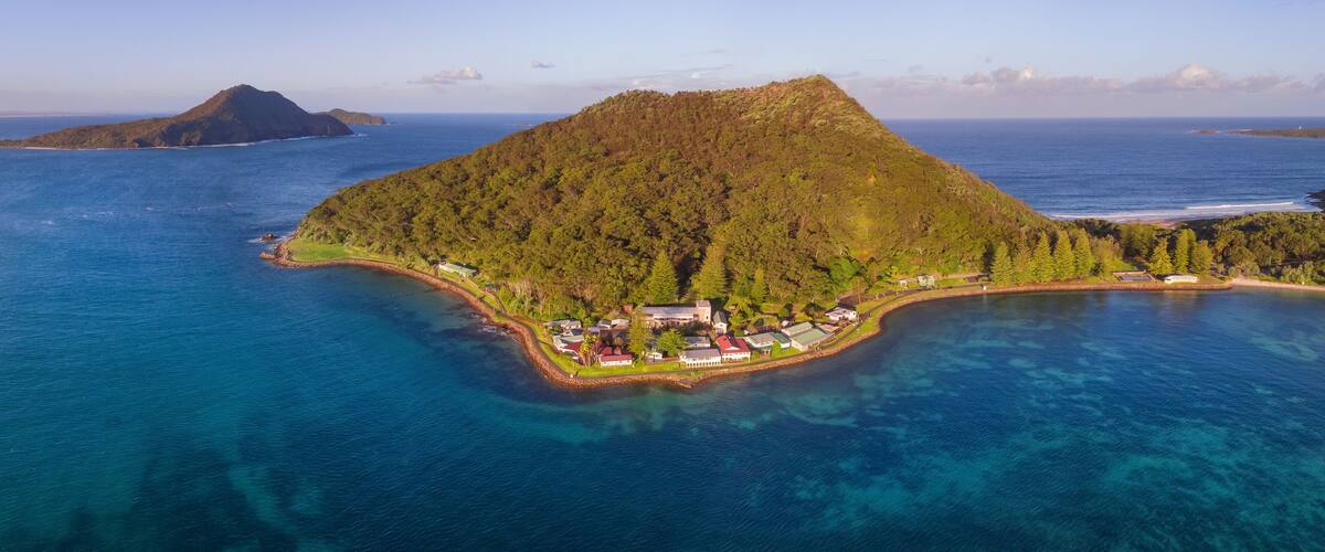 An island with a dense forest, a small settlement, and clear blue waters.