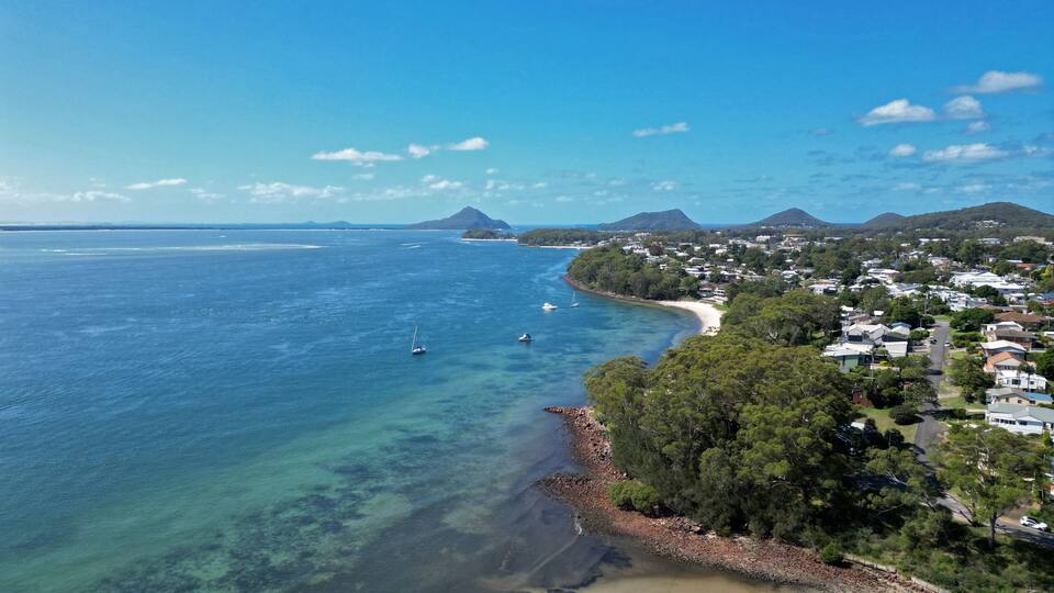 A coastal town with clear blue waters, a sandy beach, and a backdrop of green hills.