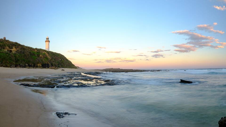 A beach with a lighthouse, waves, and a clear sky.