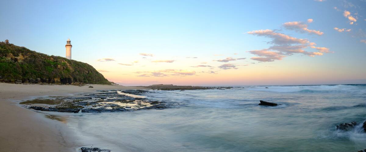 A beach with a lighthouse, waves, and a clear sky.