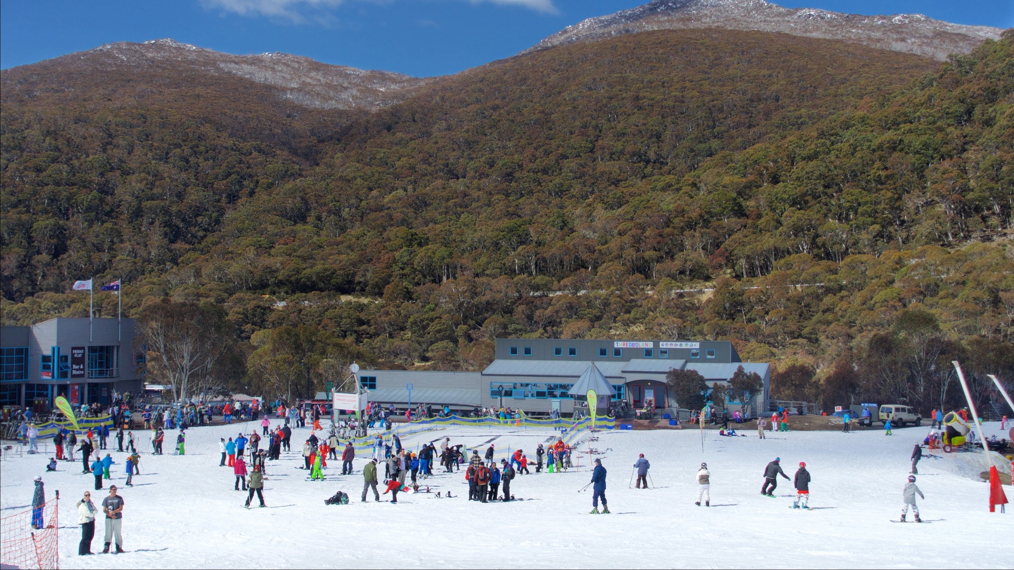 A ski resort with a crowd of people on the slopes, a building labeled "Tredboland," and a forested mountain in the background.
