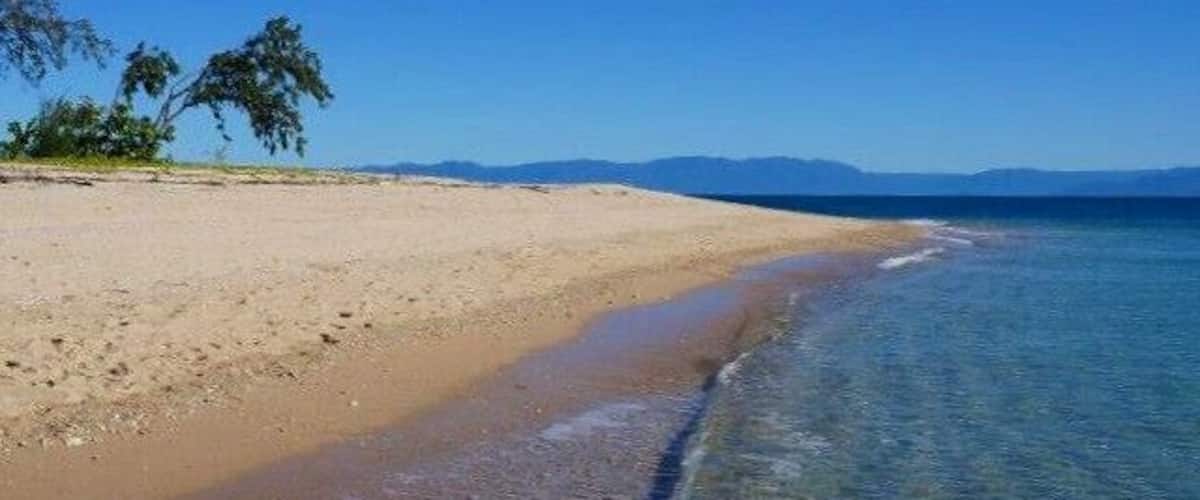 A beach with clear water, sandy shore, and distant mountains.