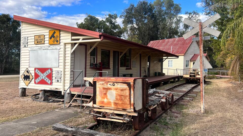 A vintage railway station with a caboose, a red-roofed building, and a railway crossing sign.