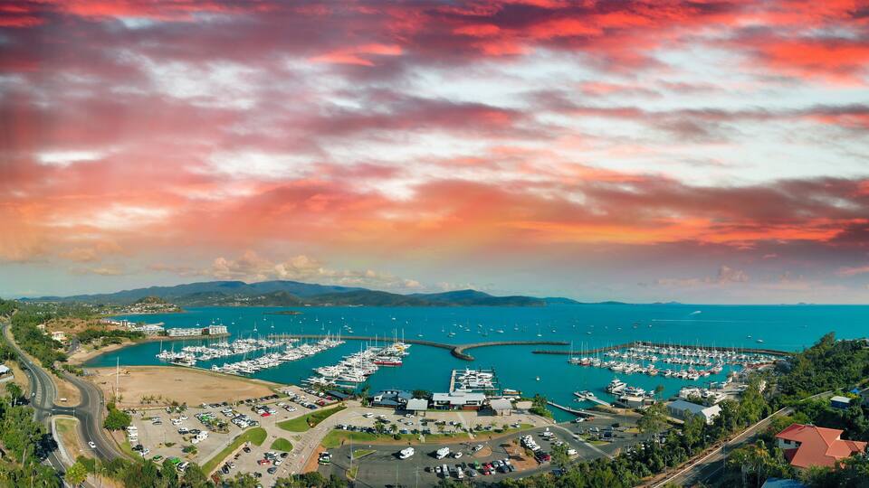 A marina with numerous boats, a parking lot, and a coastal road.