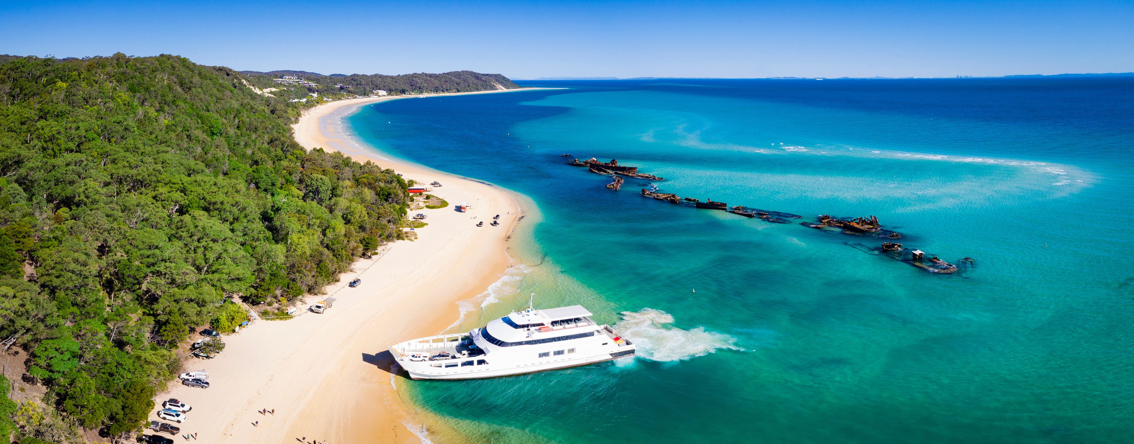 A coastal landscape with a beach, a boat, and a forested area.