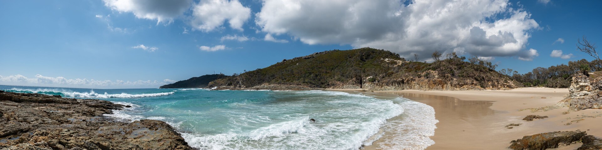A coastal landscape with rocky shores, a sandy beach, and a hill with sparse vegetation.