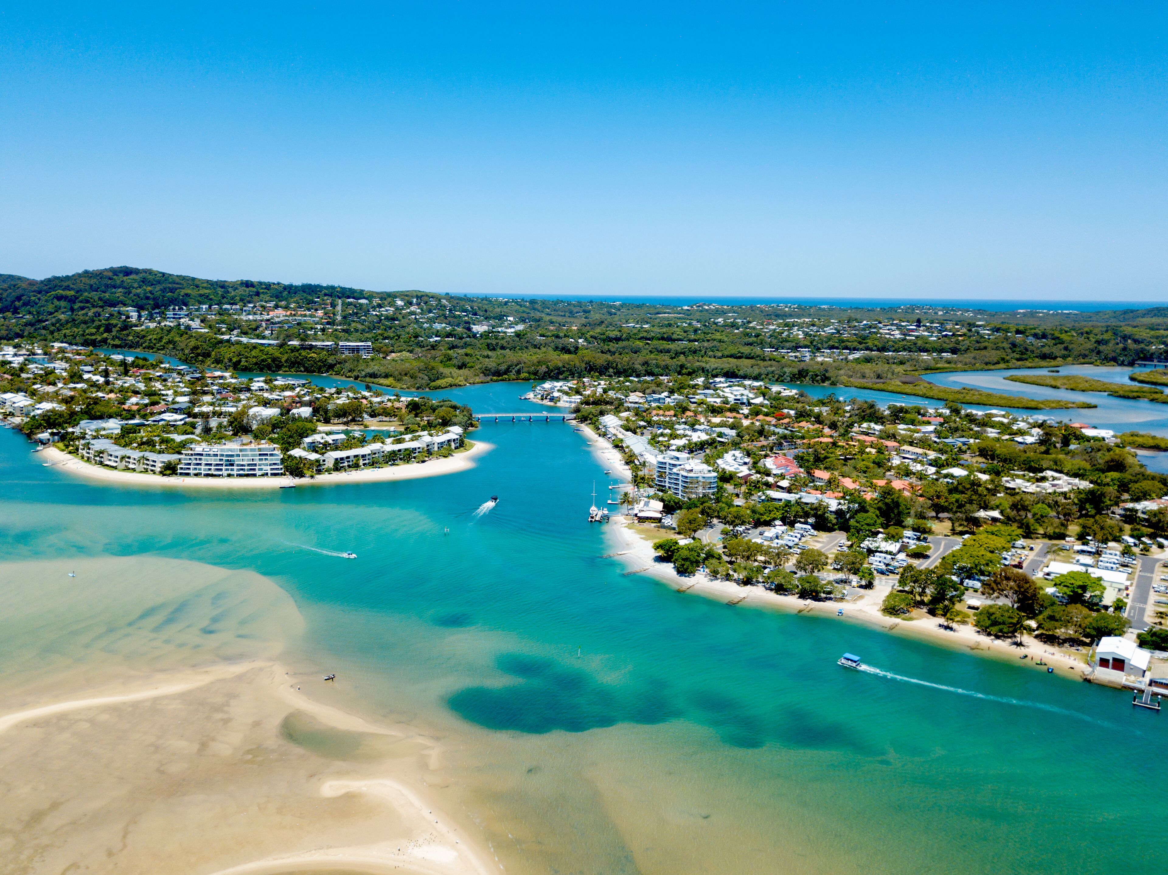 An aerial view of a coastal town with a marina, sandy beaches, and lush greenery.