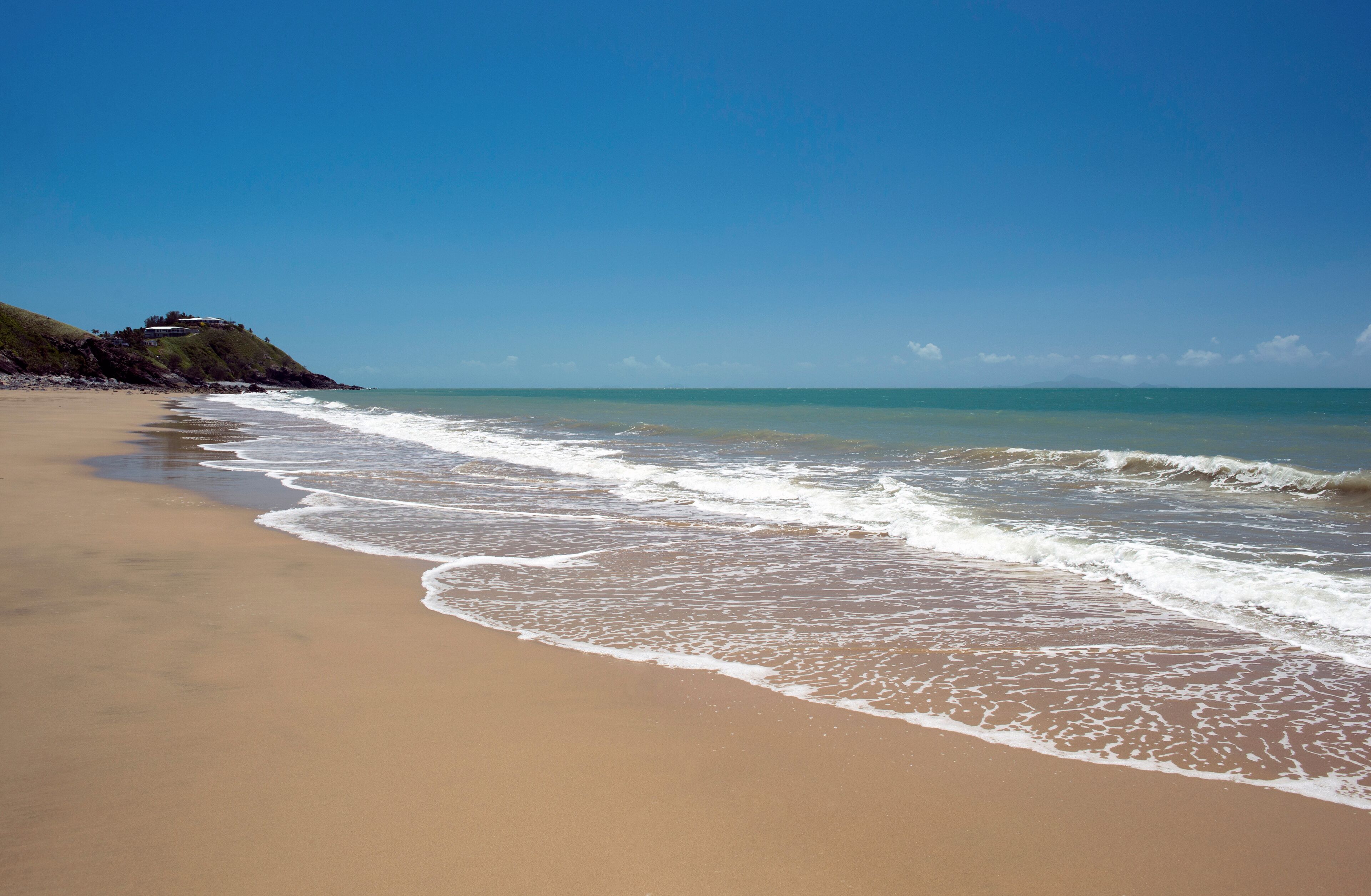 A sandy beach with gentle waves and a clear blue sky.