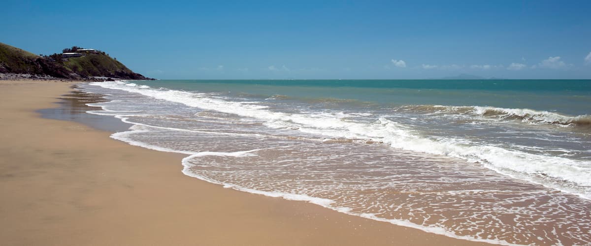 A sandy beach with gentle waves and a clear blue sky.