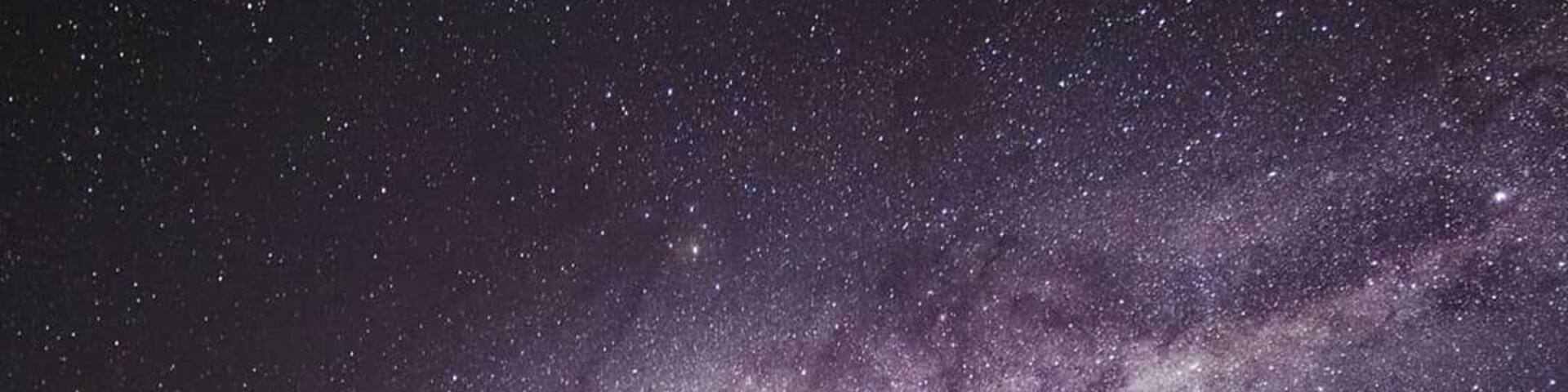 Una persona de pie sobre una duna bajo un cielo nocturno estrellado, con la Vía Láctea visible.