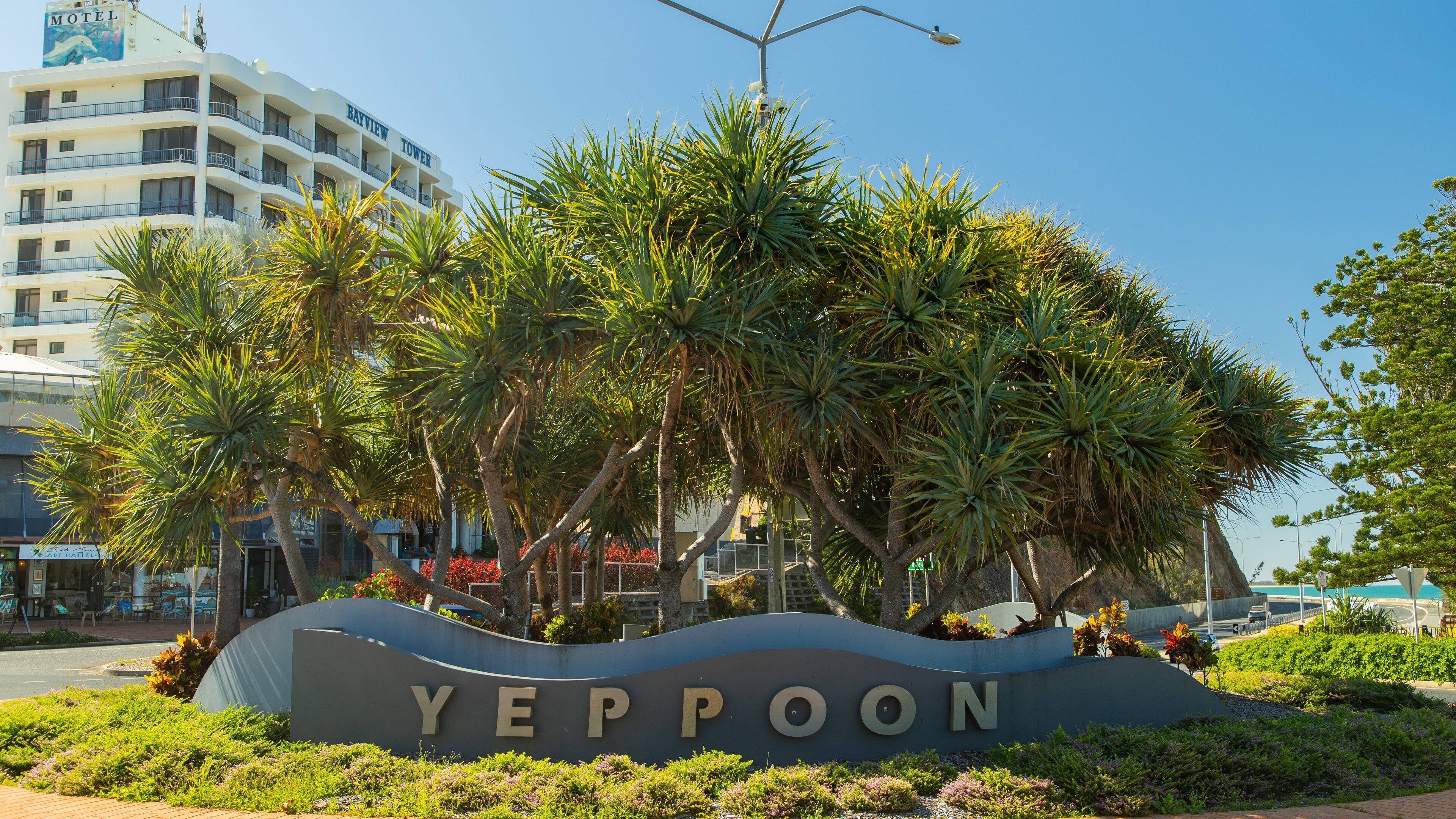 A sign for YEPPOON with palm trees and a building in the background.