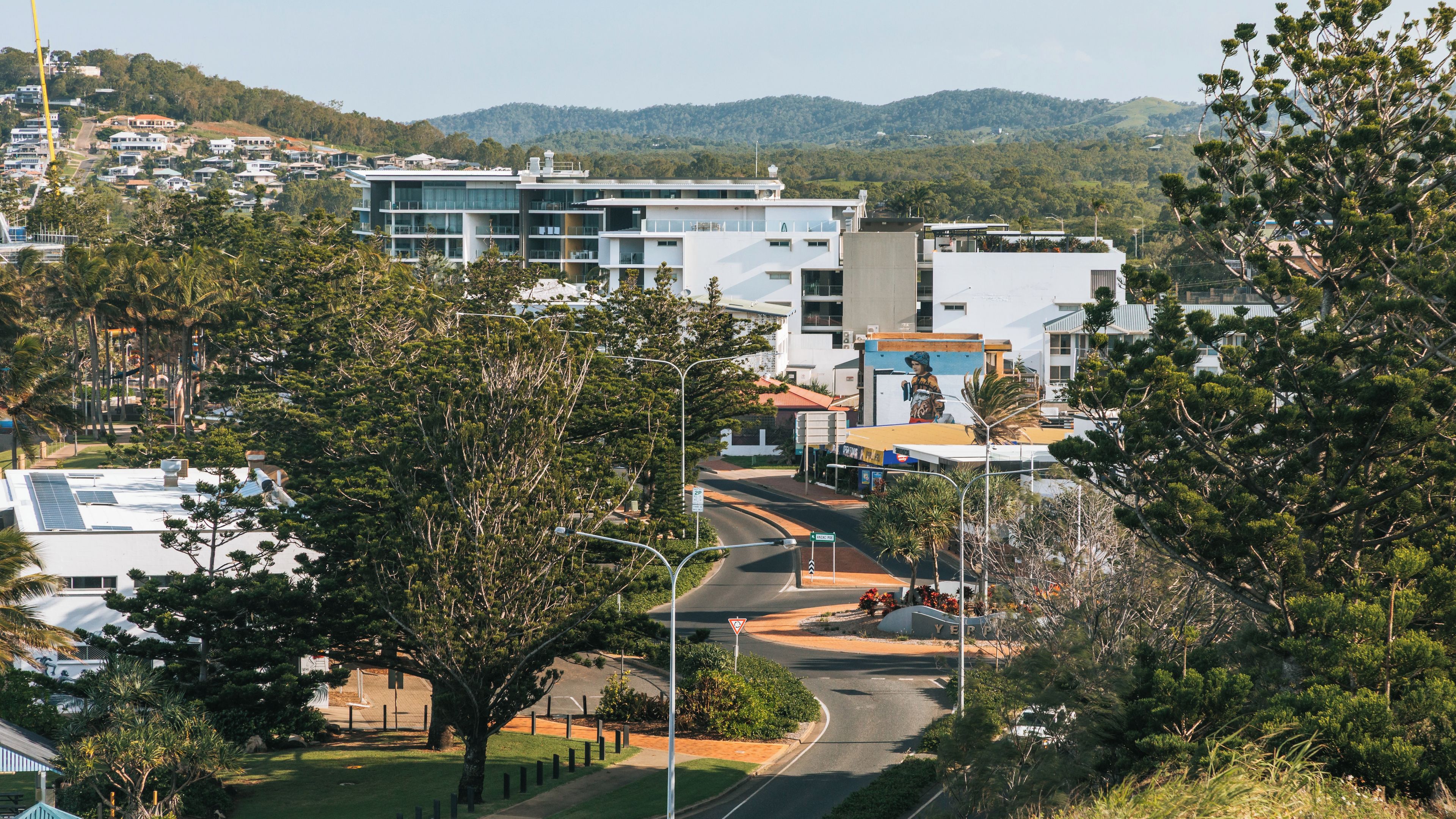 Bairro residencial com edifícios modernos, estrada sinuosa e colinas ao fundo.