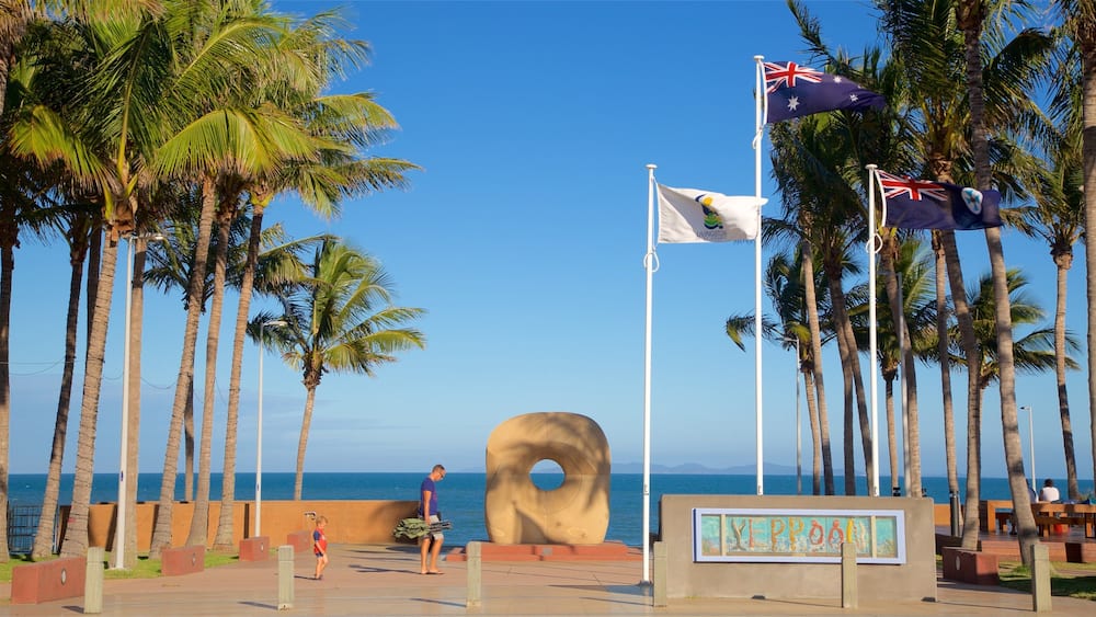 Une plage bordée de palmiers, une grande sculpture en forme de beignet et des drapeaux de l’Australie et de la Nouvelle-Zélande.