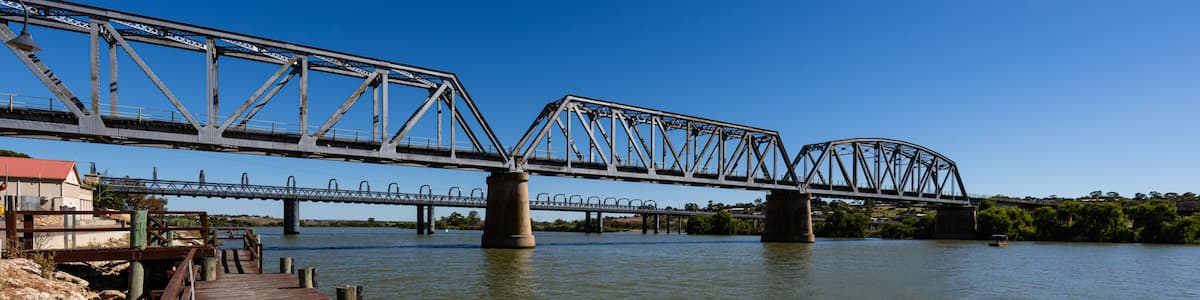 A wooden pier leading to a steel bridge over a river.