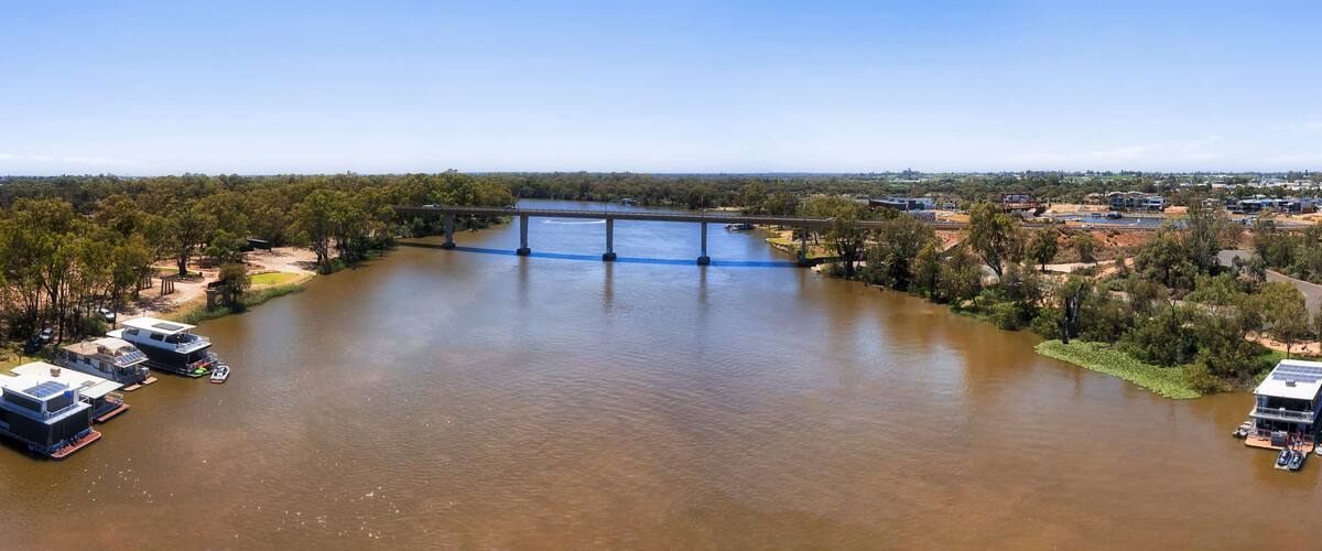 A river with a bridge, boats, and a residential area with houses and greenery.