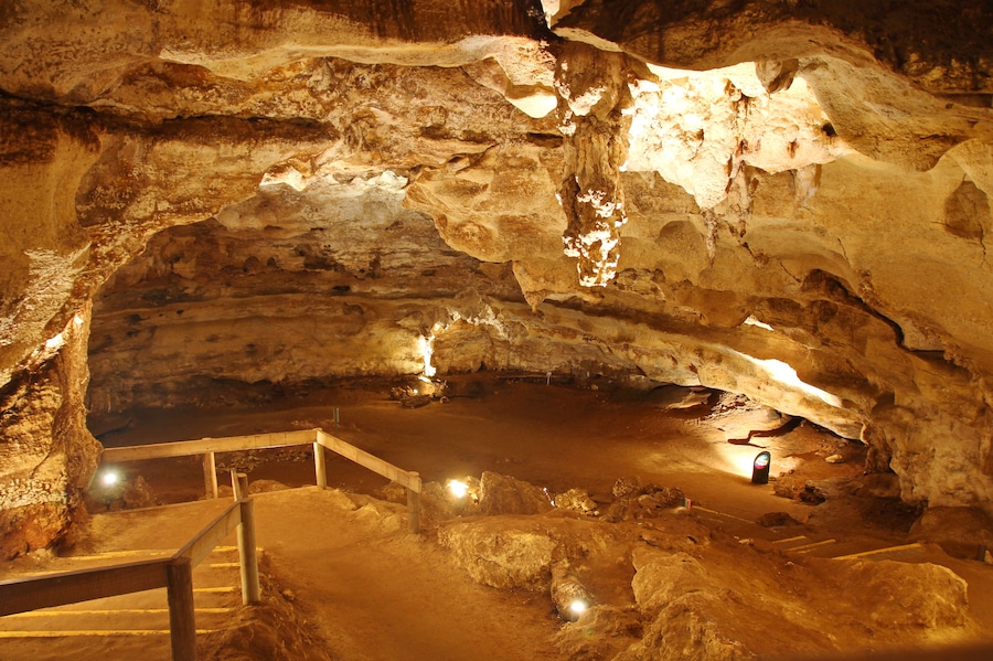 Una cueva con un pasillo de madera y una pequeña poza de agua.