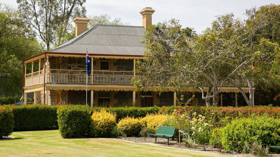 A large, two-story building with a balcony, surrounded by well-maintained gardens and trees.