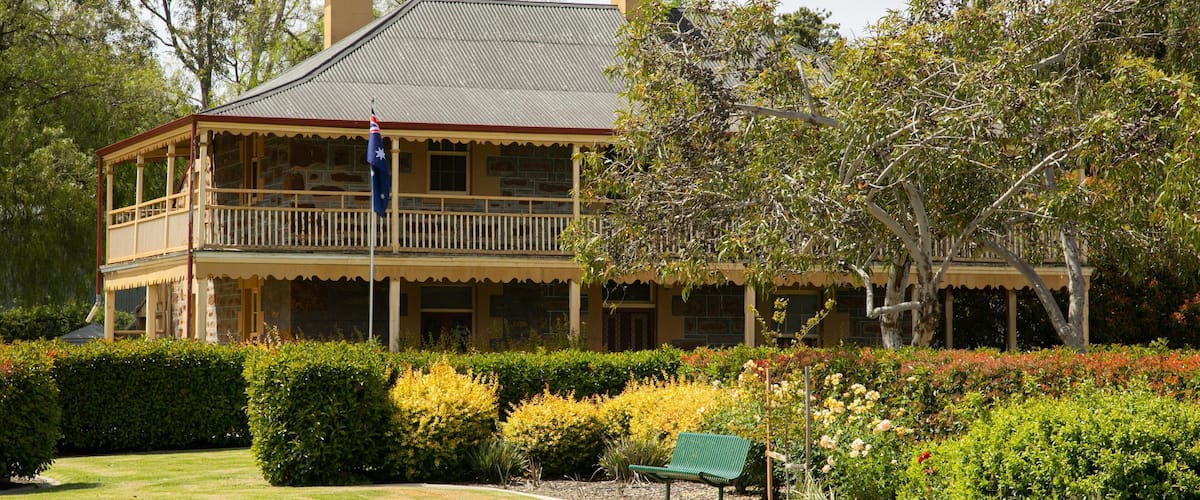 A large, two-story building with a balcony, surrounded by well-maintained gardens and trees.