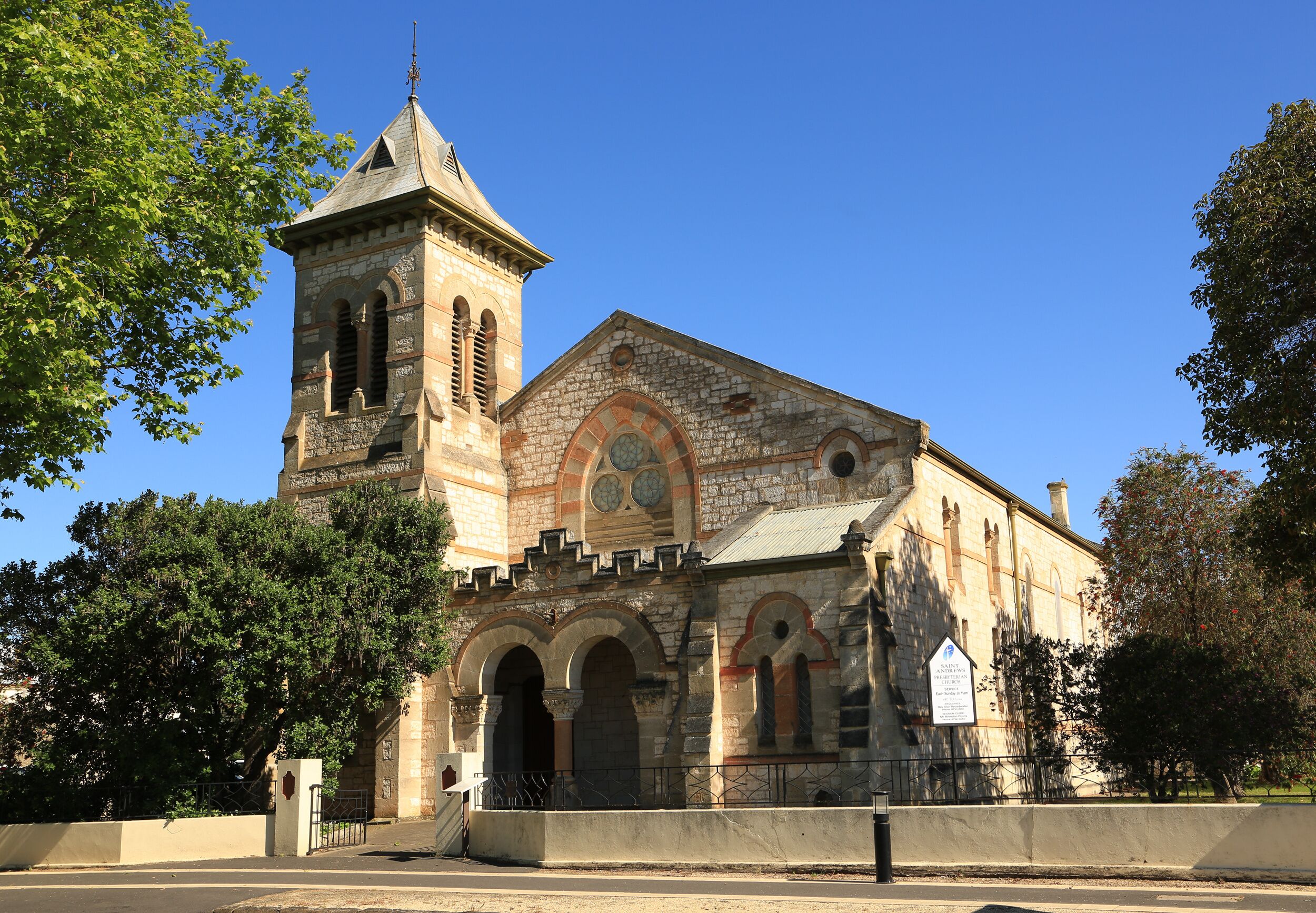 Una iglesia de piedra histórica con una torre de campanas, ventanas en arco y un cielo azul despejado.
