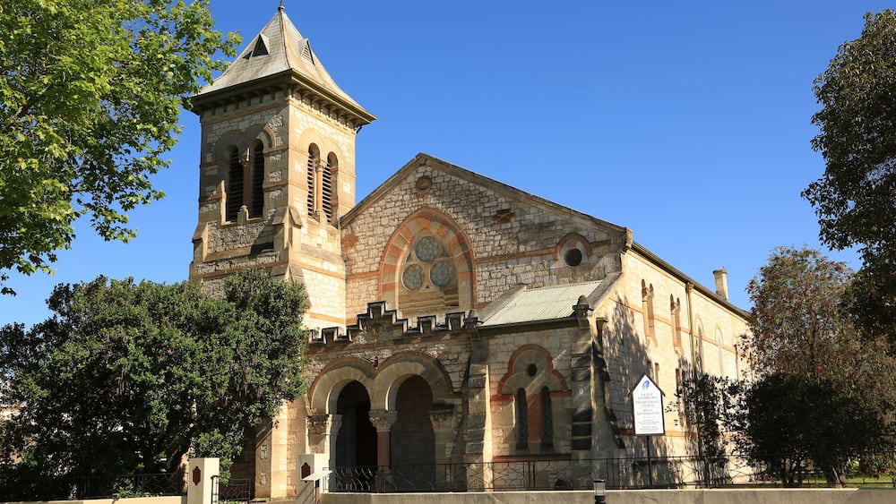 A historic stone church with a bell tower, arched windows, and a clear blue sky.