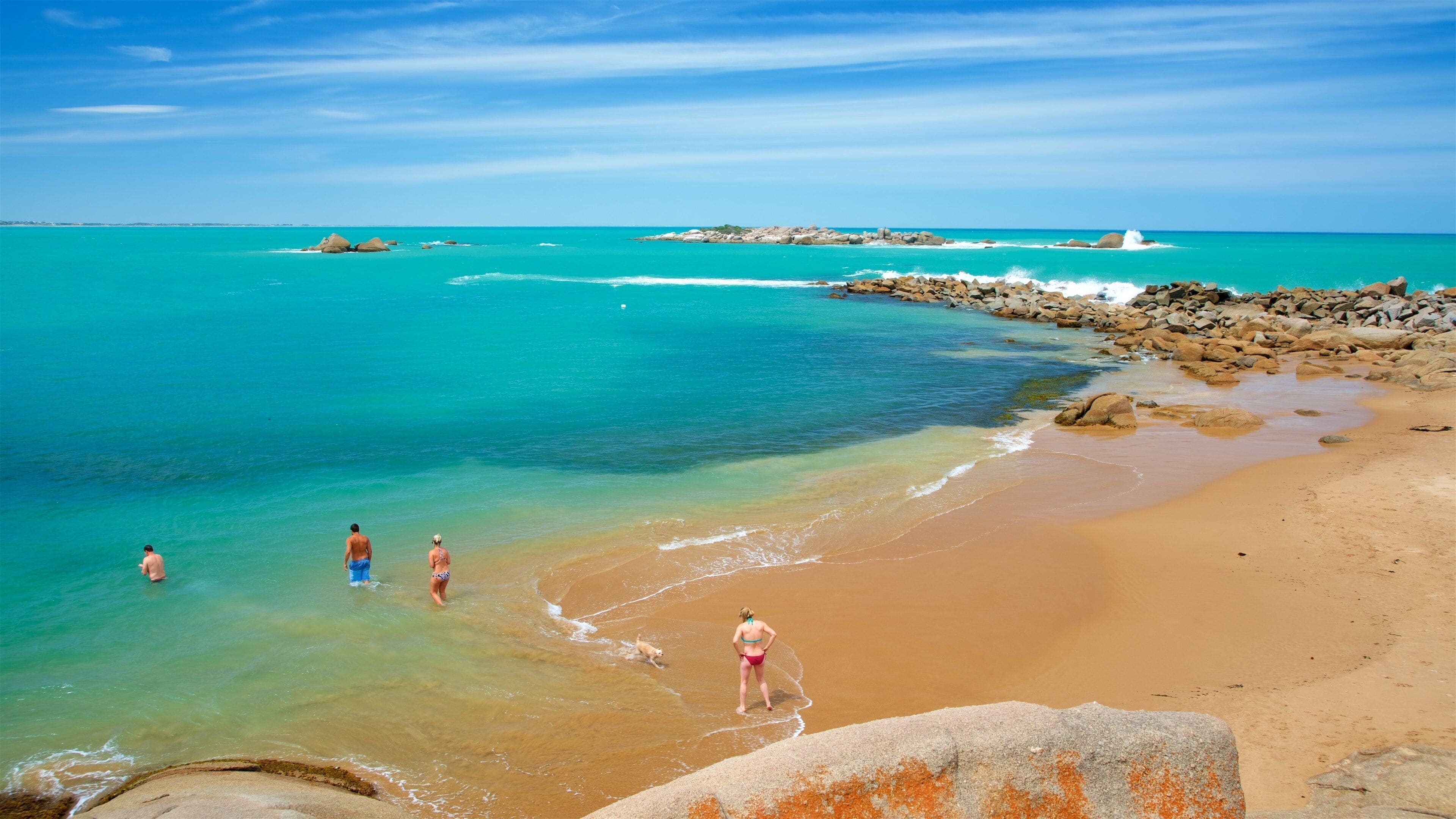 A beach with clear turquoise water, a sandy shore, and rocky outcrops.