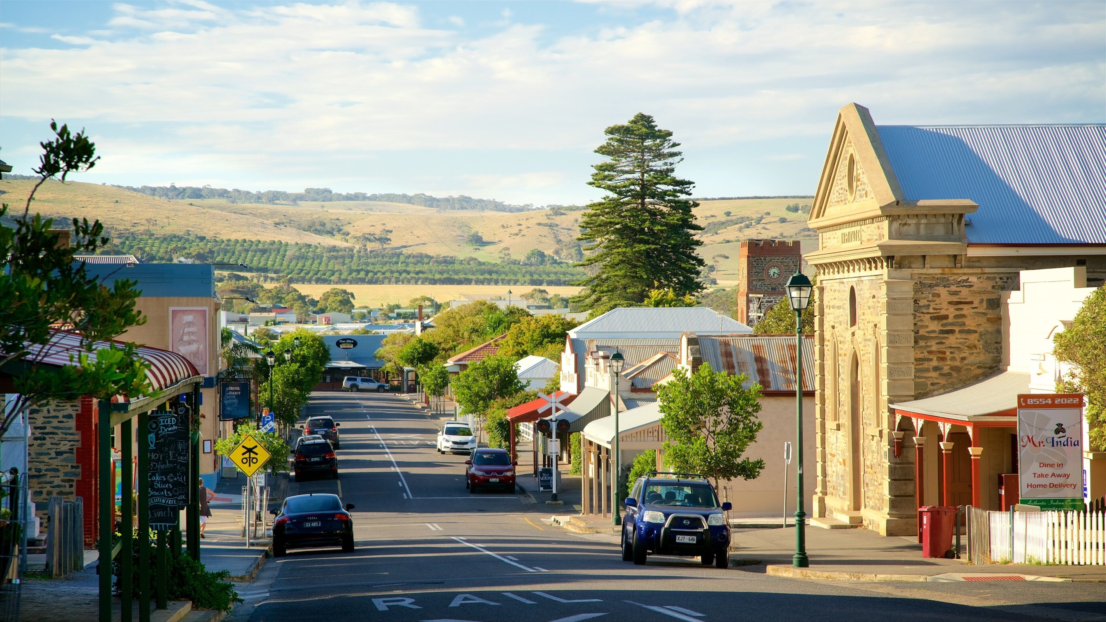 A street in a small town with buildings, cars, and a hill in the background.