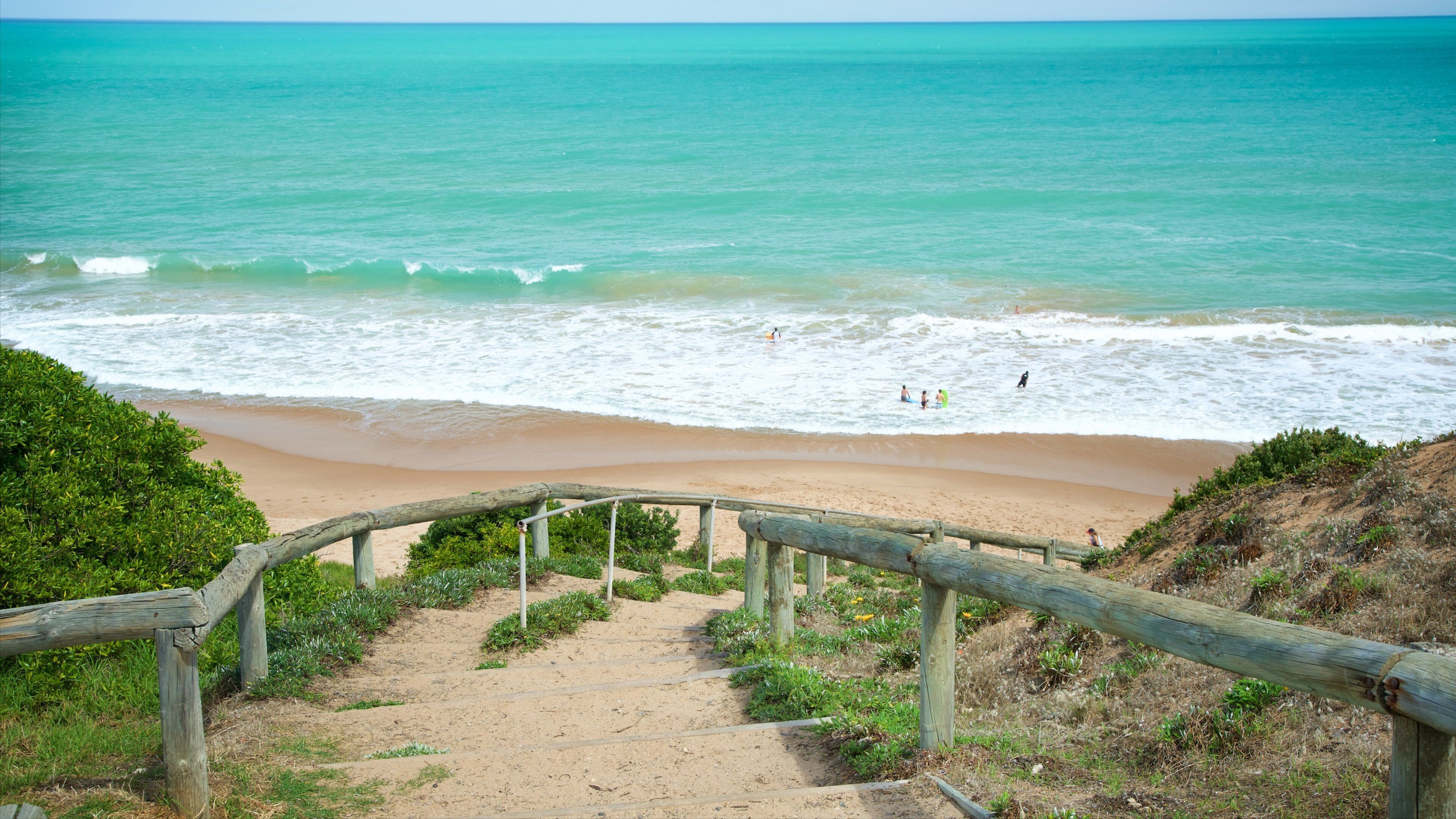 A sandy beach with a wooden staircase leading down to the water, surrounded by greenery.