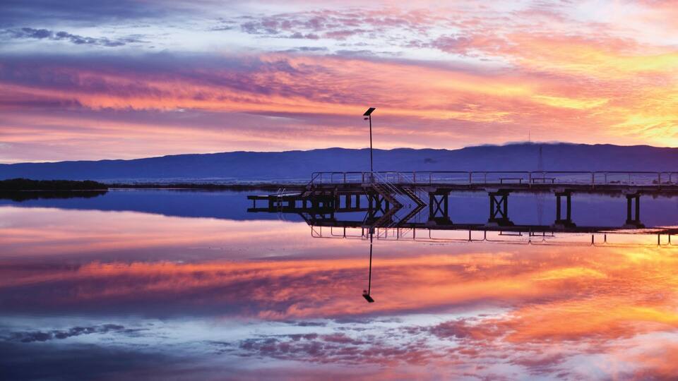 A sunset over a calm lake with a dock and mountains in the background.