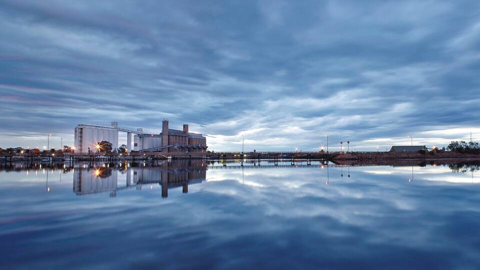 A large industrial facility with multiple silos and a bridge over a calm body of water.