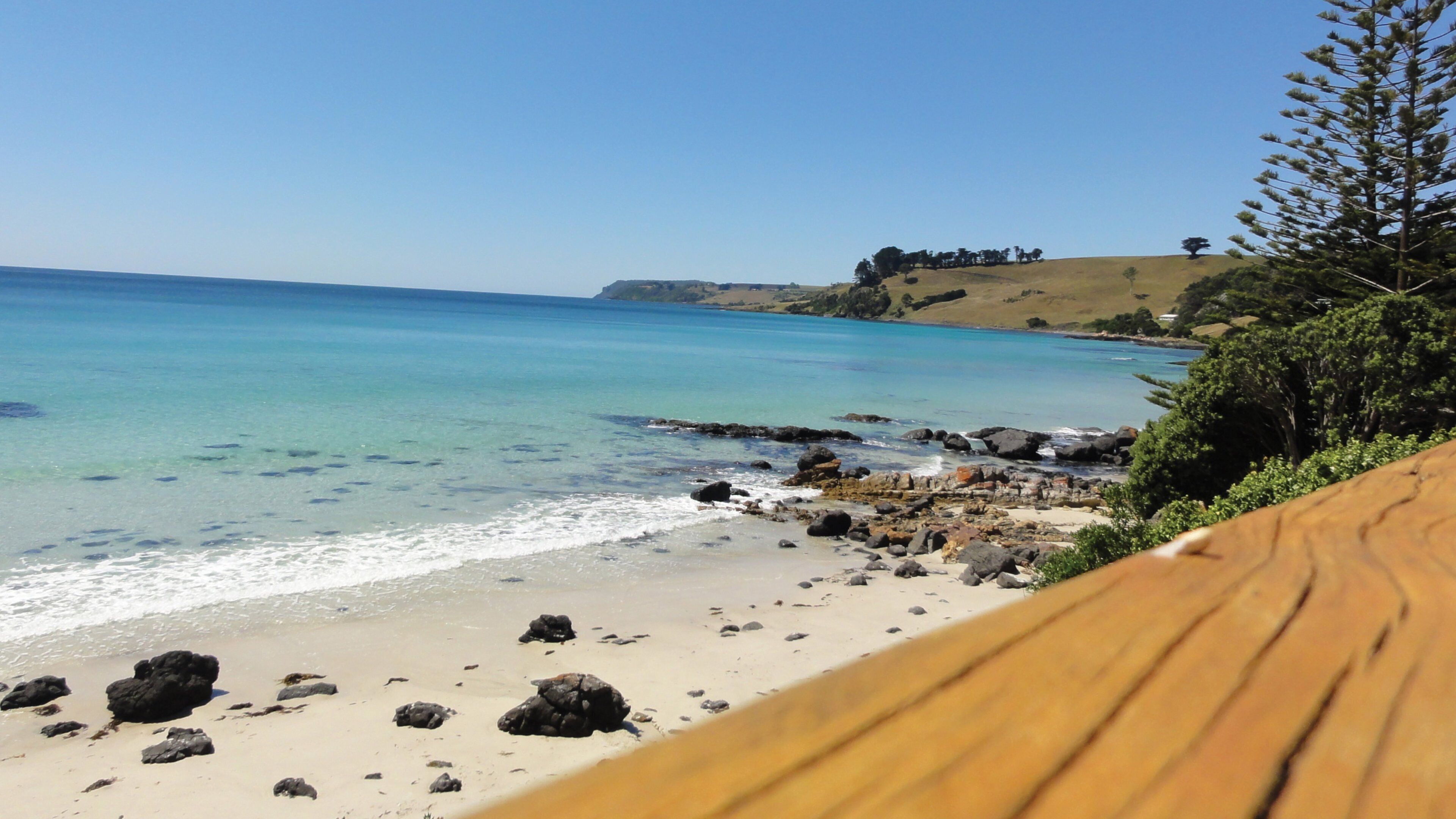 A beach with clear turquoise water, rocky shoreline, and a wooden deck.