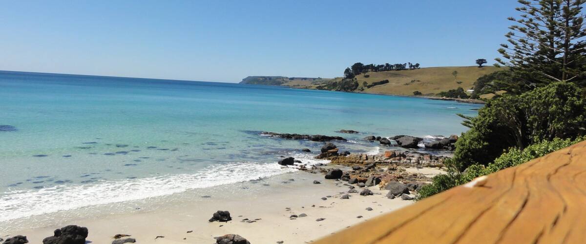 A beach with clear turquoise water, rocky shoreline, and a wooden deck.