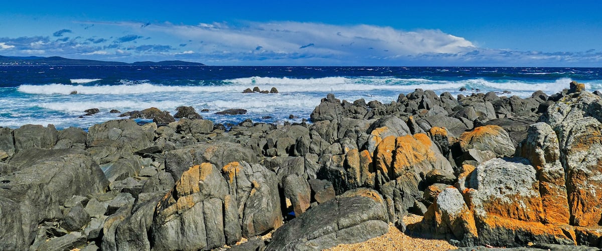 A rocky coastline with waves crashing against the rocks under a clear blue sky.