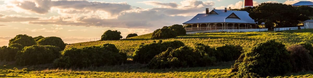 A lighthouse, a white house with a blue roof, and a grassy field under a clear sky.