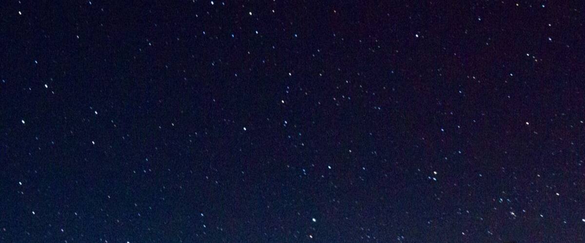 A starry night sky over a grassy field with a tree and a tower.