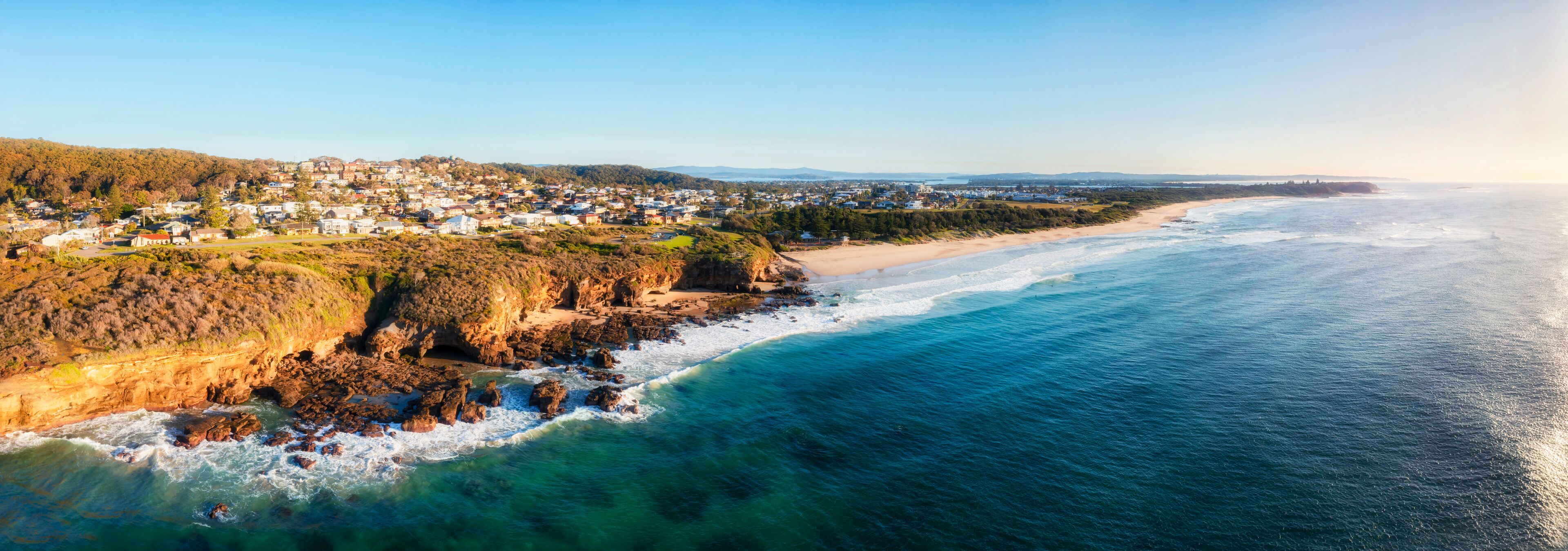 A coastal town with a beach, rocky cliffs, and a clear view of the ocean.